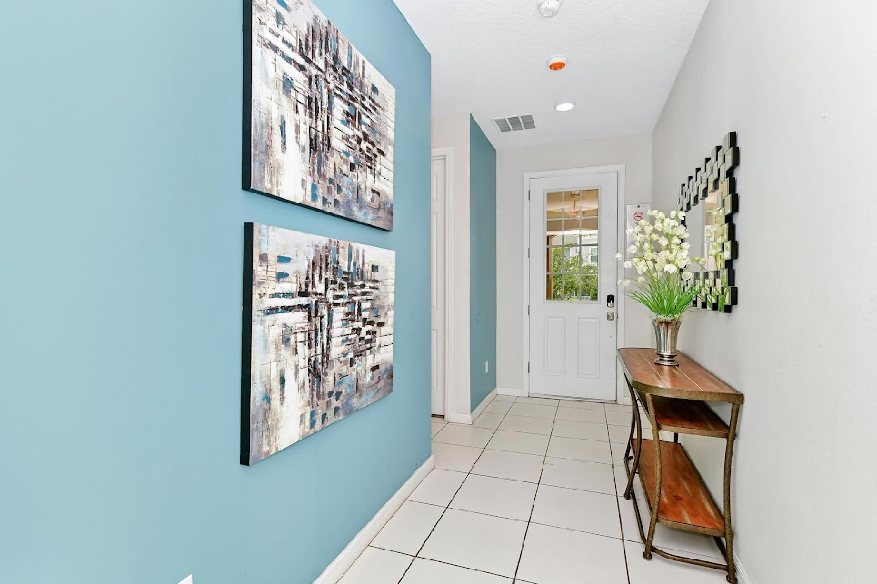 A hallway with two abstract paintings on the wall, a white door, and a small table with a vase of flowers.