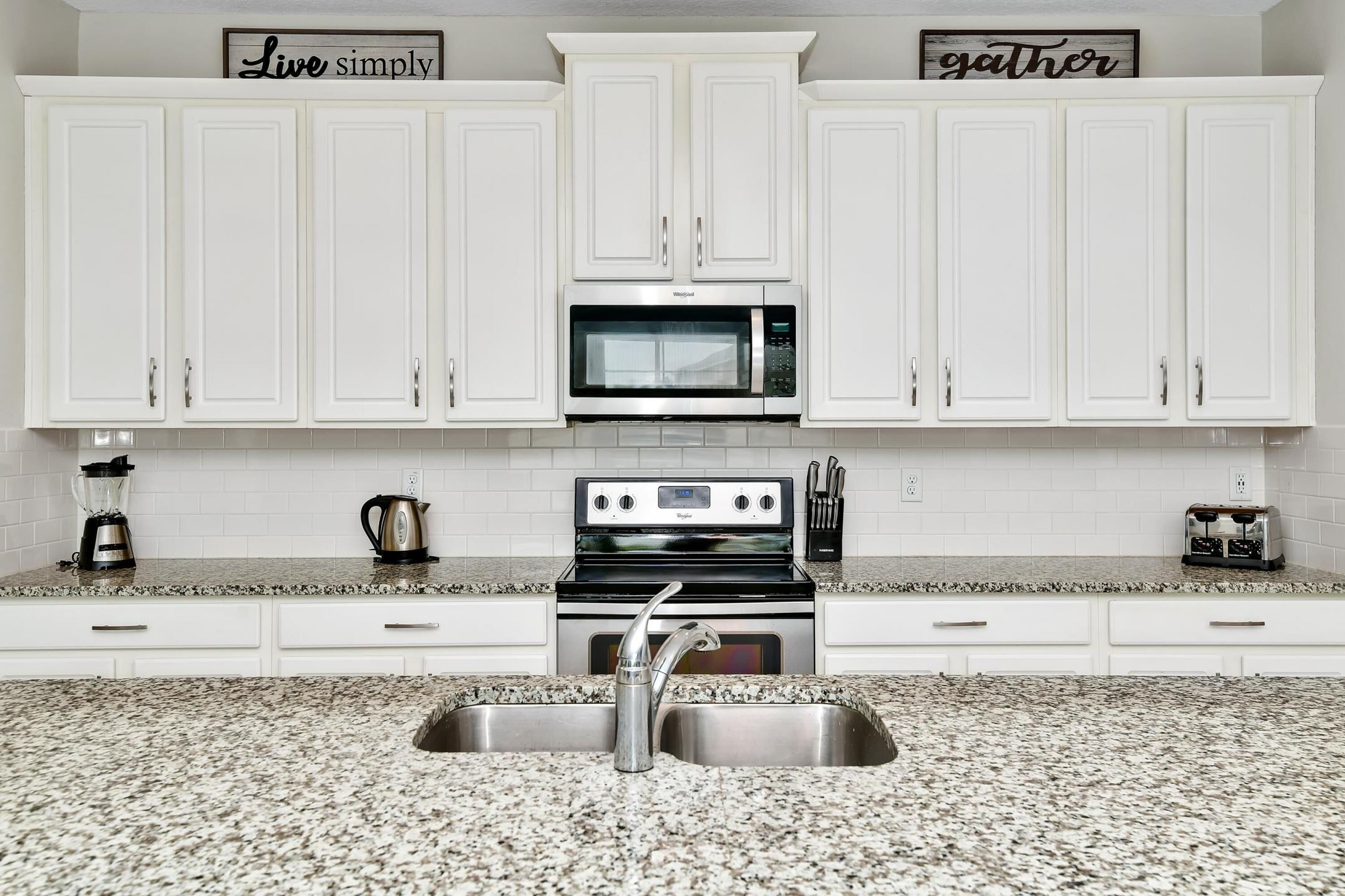 A kitchen with white cabinets, a microwave, a stove, and a sink.