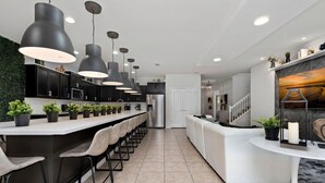 A modern kitchen with a central island, black pendant lights, and a white staircase. - Sleeps 20 - Masterpiece Collection Ww101 (Kissimmee)