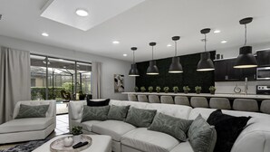 A modern living room with a sectional sofa, a coffee table, and a kitchen area with pendant lighting. - Sleeps 20 - Masterpiece Collection Ww101 (Kissimmee)