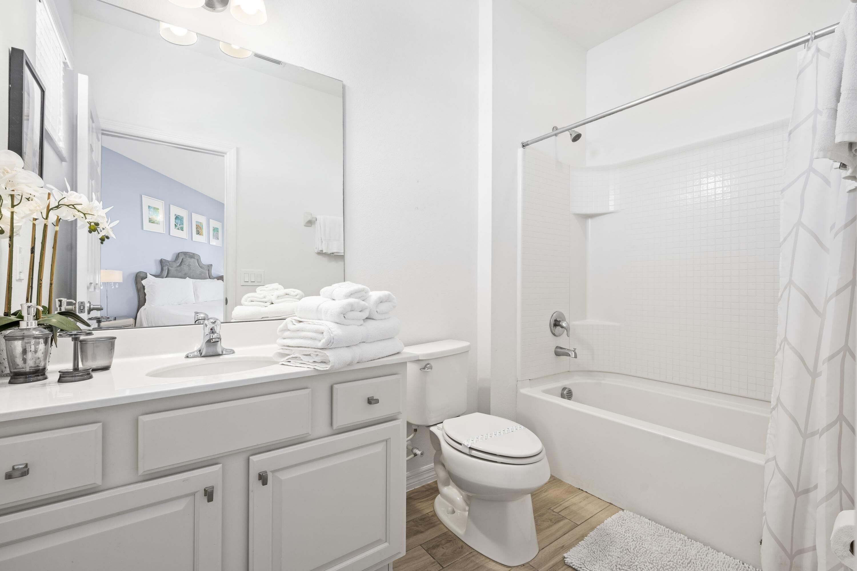 A modern bathroom with a white sink, toilet, and bathtub. There are towels stacked on the sink, and a shower curtain with a geometric pattern.