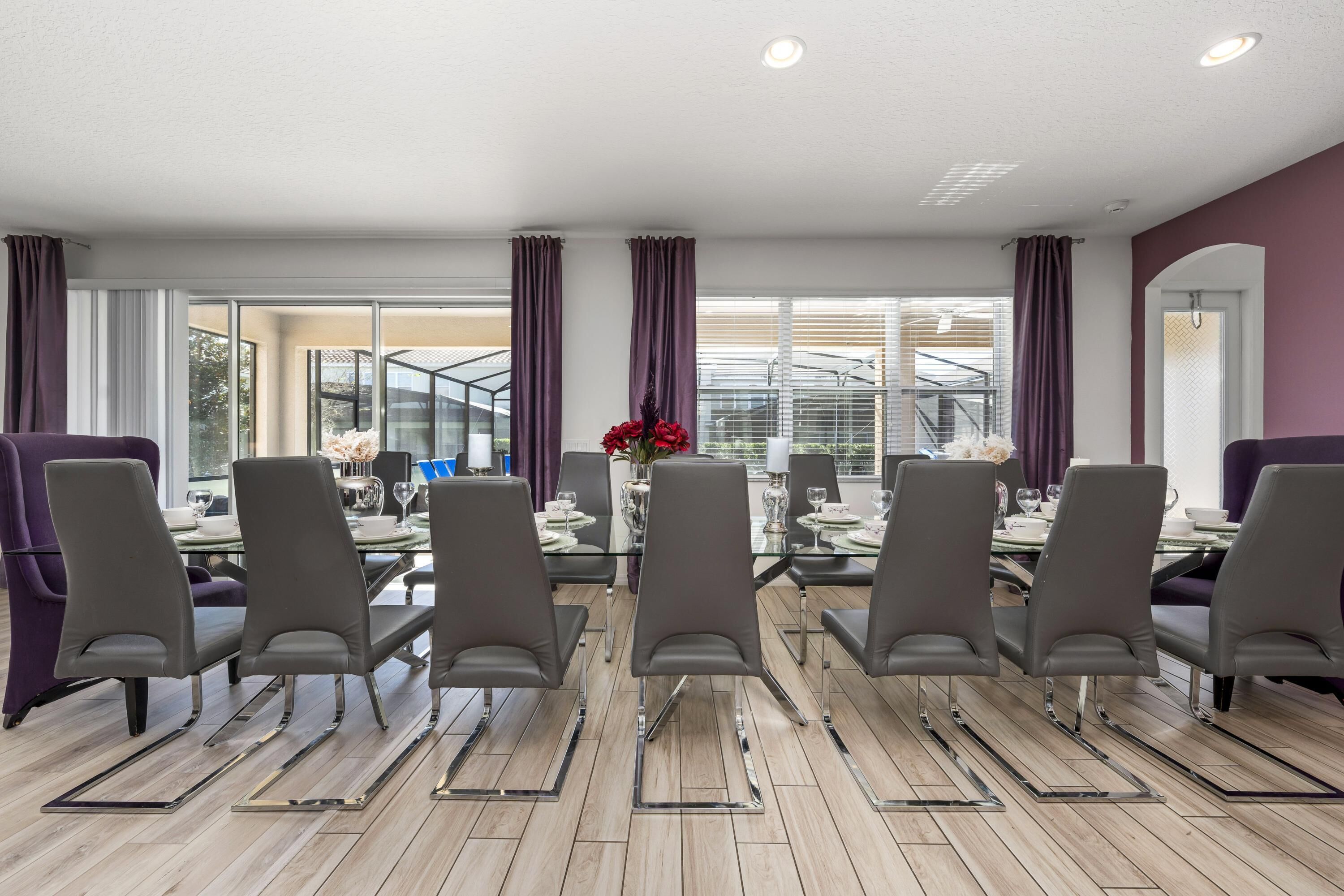 A modern dining area with a glass table, grey chairs, and purple curtains.