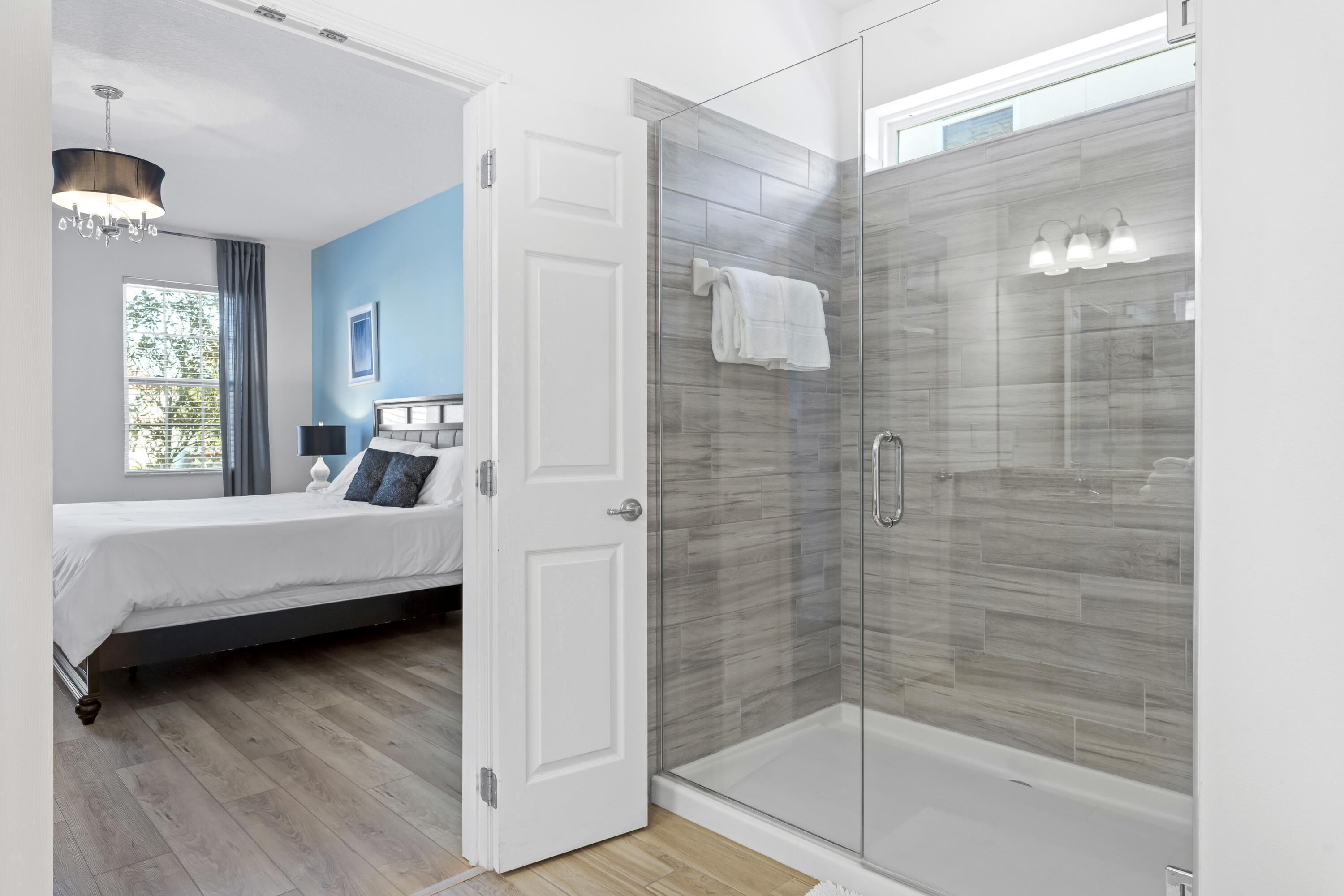 A modern bedroom with a large bed, a glass shower enclosure, and a view of the outdoors.