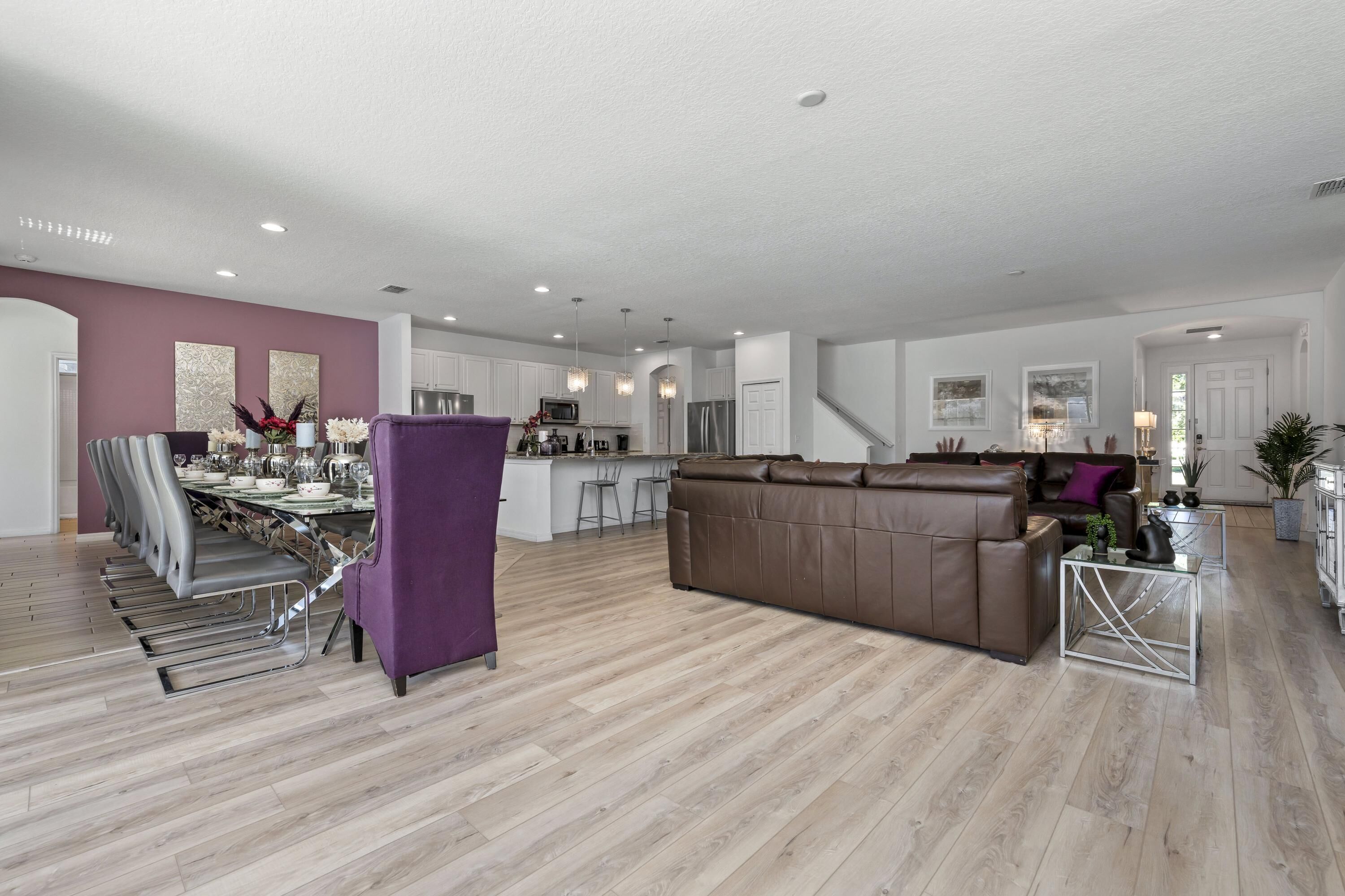 A spacious living area with a dining table, chairs, a sofa, and a kitchen in the background.