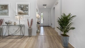 Un pasillo con una mesa de vidrio, obras de arte enmarcadas, una planta en maceta y una puerta que da a otra habitación.