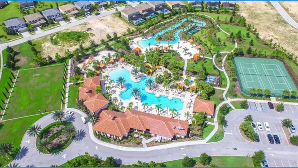 Vista aérea de un resort con una piscina central, varias villas para huéspedes, una cancha de tenis y un estacionamiento.