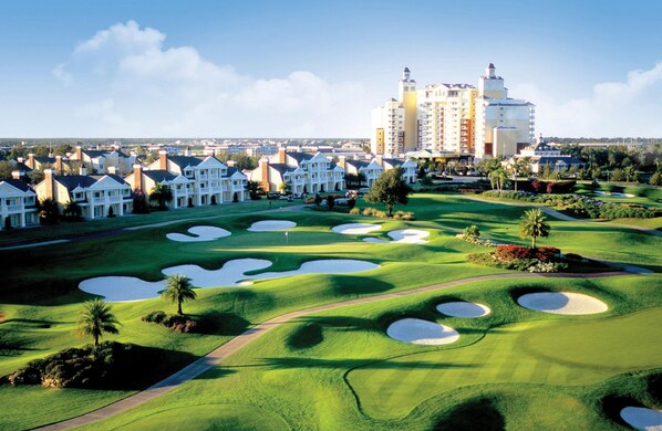 A golf course with bunkers and a large hotel complex in the background.