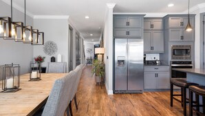 A modern kitchen with grey cabinets, stainless steel appliances, and a wooden dining table with a bench. - Entire Home in Four Corners Florida Reu101 (Kissimmee)
