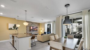 A modern kitchen with a central island, a dining area with a wooden table, and a living room with a sofa and TV. - Stylish Family Home Private Pool Stl111 (Kissimmee)