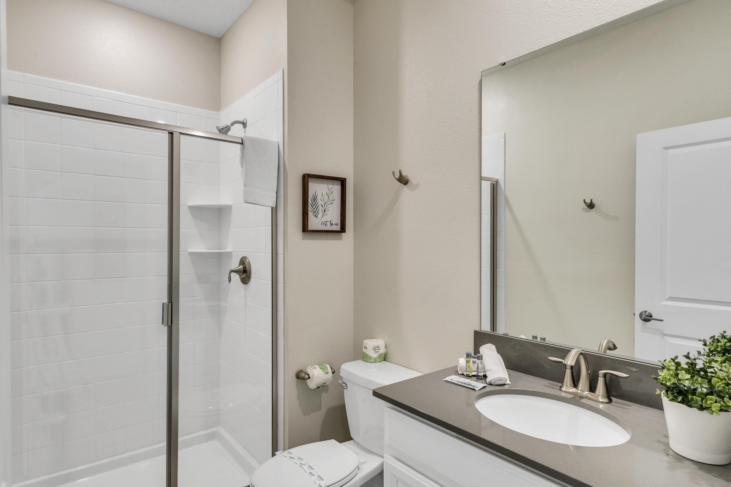 A bathroom with a glass shower enclosure, a toilet, a sink with a mirror, and a potted plant.