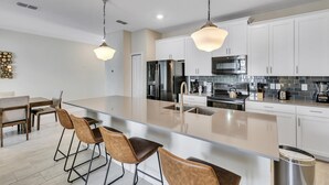 A modern kitchen with a large island, white cabinets, stainless steel appliances, and pendant lighting. - Stylish Family Home Private Pool Stl111 (Kissimmee)