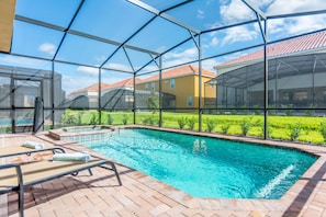 An indoor swimming pool with clear glass walls, a tiled deck, and lounge chairs.