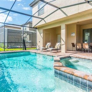 A swimming pool with a sunken hot tub, lounge chairs, and a covered patio area.