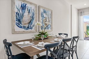 Comedor con una mesa de madera dispuesta para cuatro personas, una obra de arte enmarcada en la pared y una planta en maceta sobre la mesa.