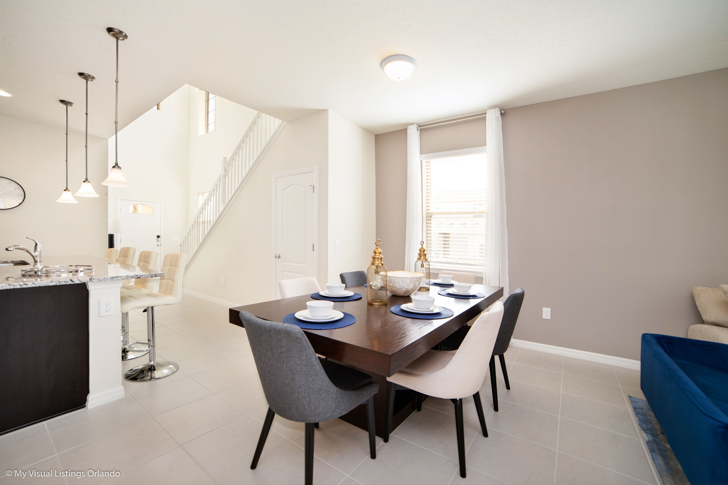 A modern dining area with a dark wooden table, white chairs, and a kitchen island with bar stools.