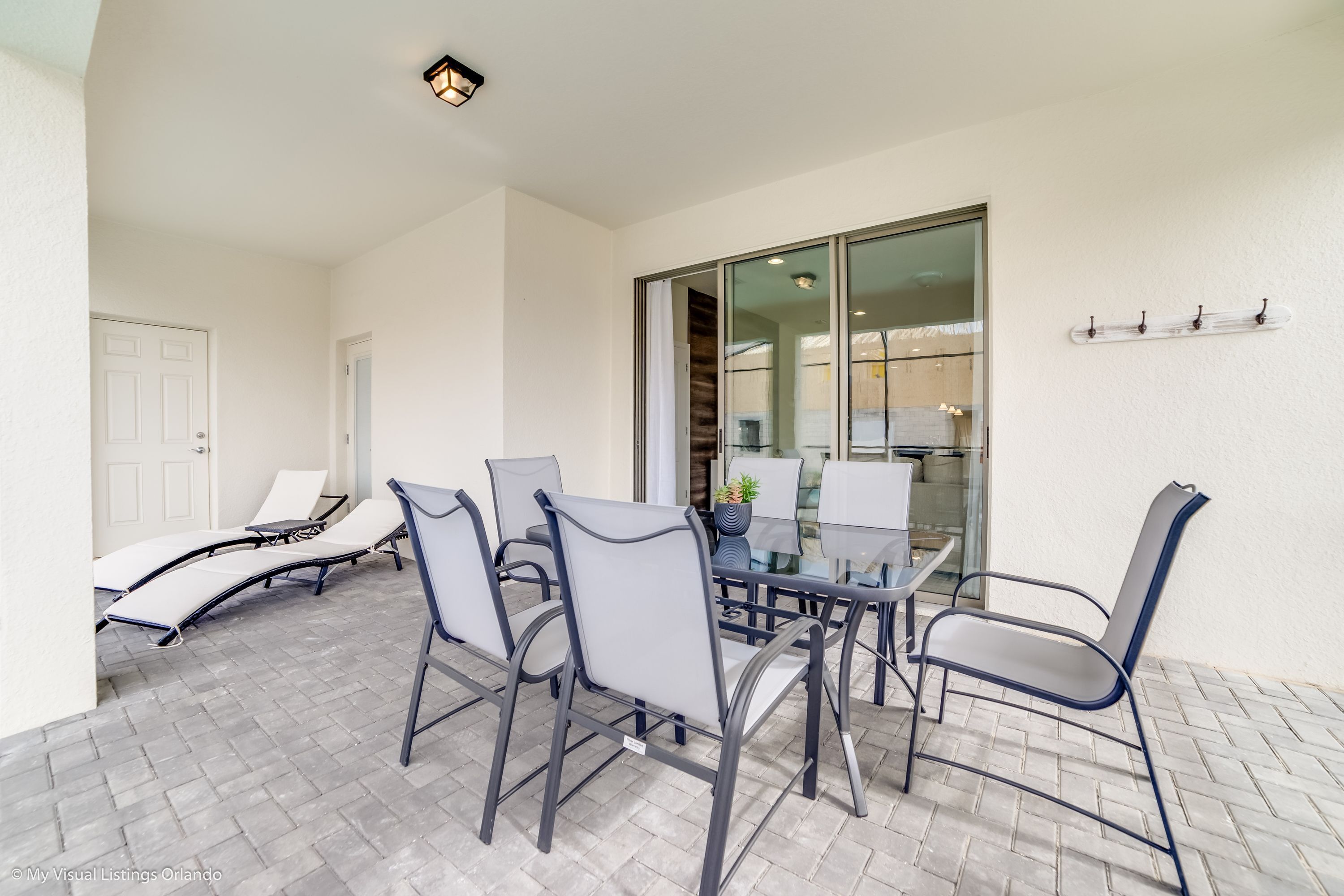 Eine Terrasse mit Glastisch und Stühlen, einer Tür und einem an der Wand befestigten Regal.