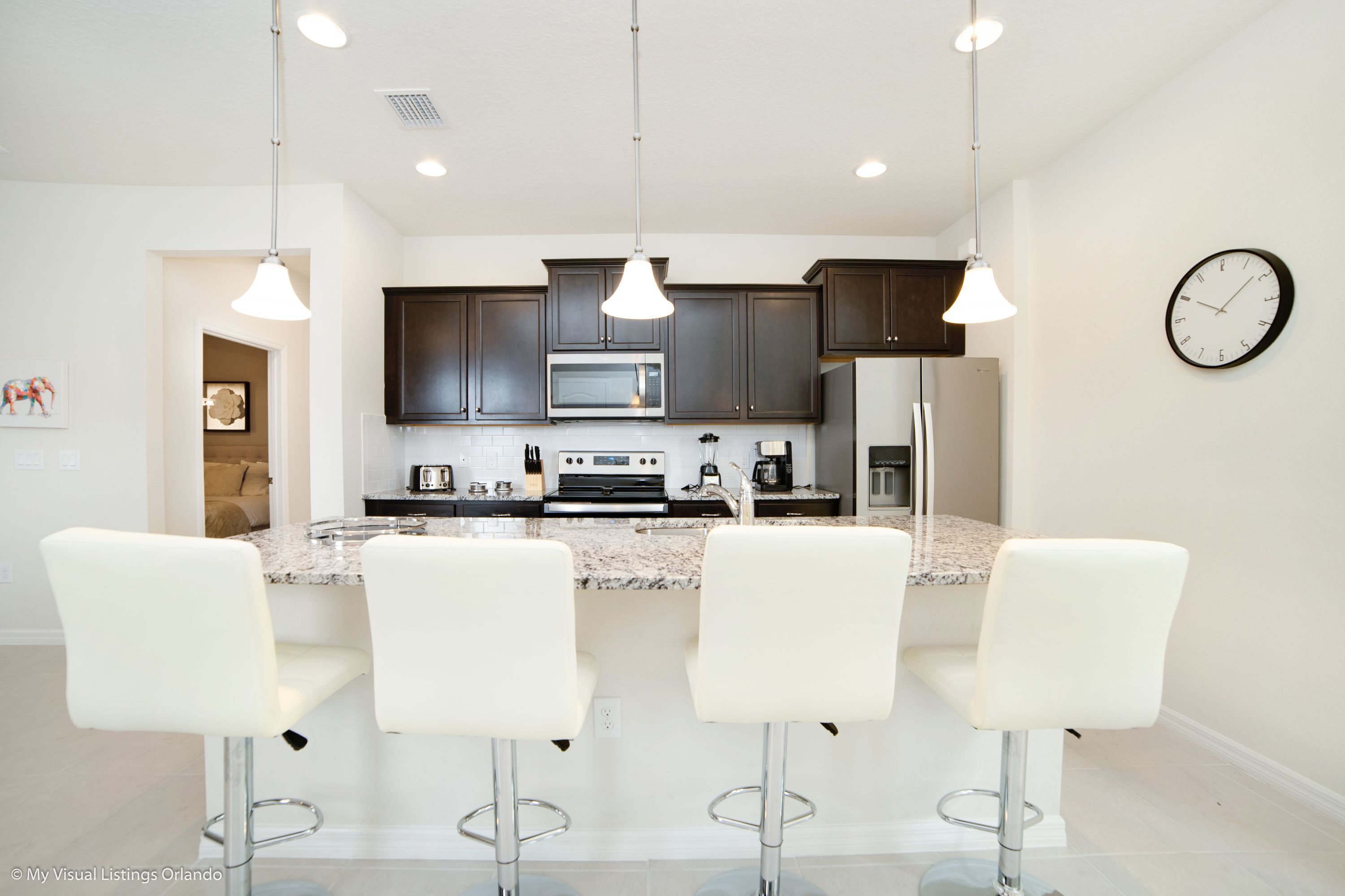 A modern kitchen with dark cabinets, a large island with bar stools, stainless steel appliances, and pendant lighting.