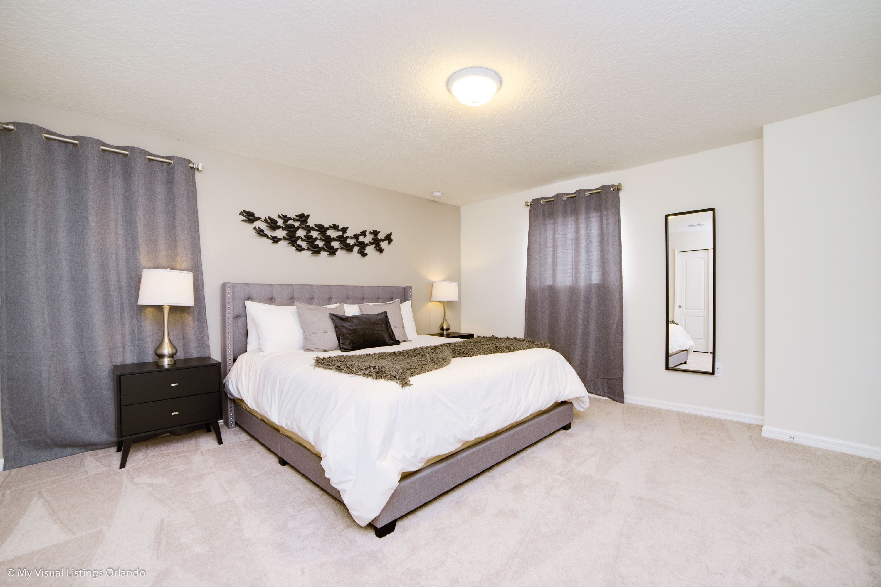 A bedroom with a large bed, two bedside tables, a wall-mounted mirror, and a ceiling light.
