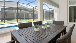 A covered patio with a wooden table and chairs, a pool in the background, and a view of a house. - Dashing Family Home Stl113 (Kissimmee)