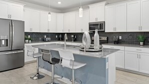 A modern kitchen with white cabinets, stainless steel appliances, and a central island with bar stools. - Dashing Family Home Stl113 (Kissimmee)