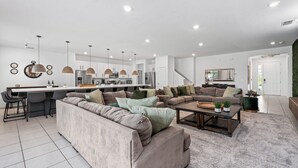 A modern living room with a large sectional sofa, a coffee table, and a dining area with bar stools. - Unique Masterpiece 15 En-suites Vpr104 (Kissimmee)