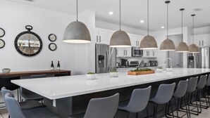 A modern kitchen with a central island, pendant lights, and a clock on the wall. - Unique Masterpiece 15 En-suites Vpr104 (Kissimmee)