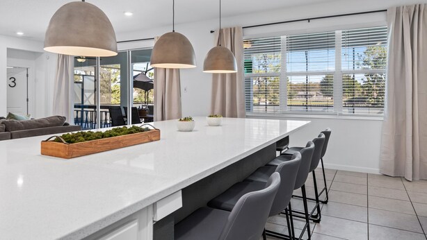 A modern kitchen with a large island, pendant lights, and a view of the outdoors through large windows. - Unique Masterpiece 15 En-suites Vpr104 (Kissimmee)