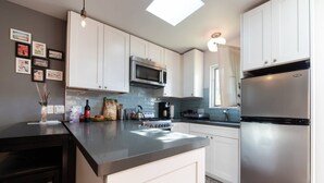 Une cuisine moderne avec des meubles blancs, un réfrigérateur en acier inoxydable et une cuisinière à gaz.