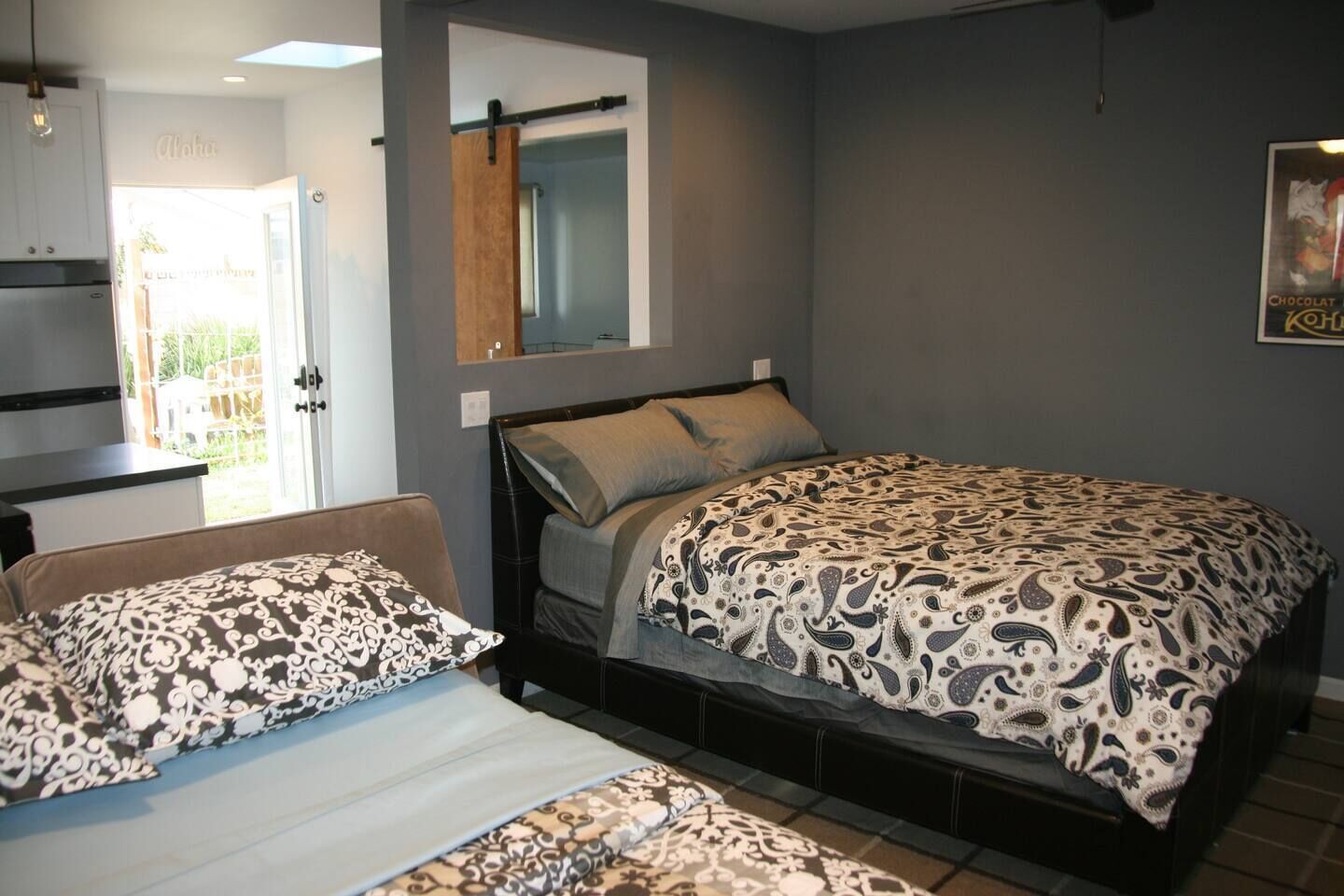 A bedroom with a bed, a chair, a mirror, and a door leading to an outdoor area.