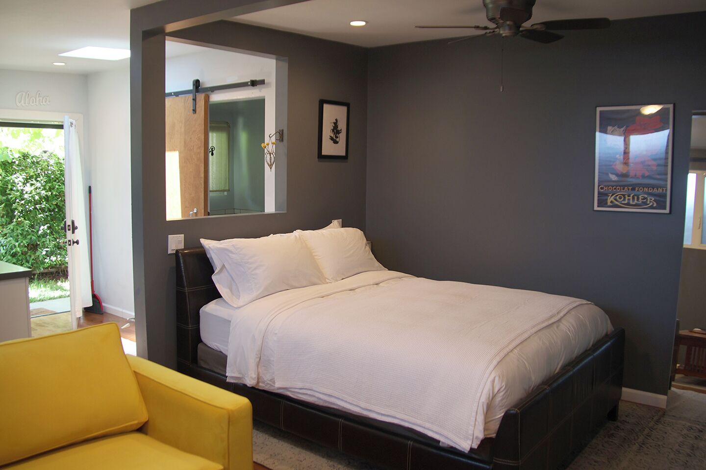 Un dormitorio con cama, un sillón amarillo, un ventilador de techo y un cartel en la pared.
