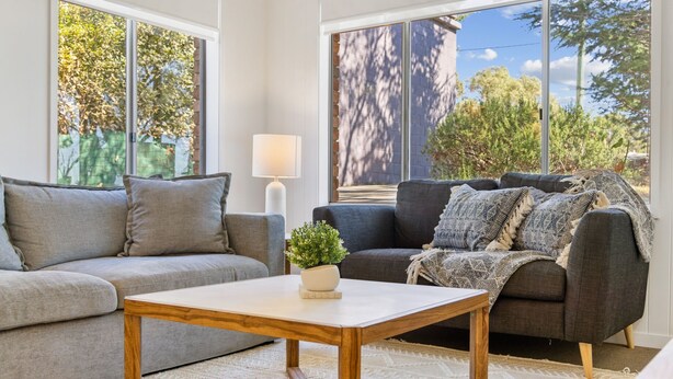 Ein Wohnzimmer mit grauem Sofa, einem dunkleren Sofa mit gemustertem Überwurf, einem Holztisch und einer Stehlampe.