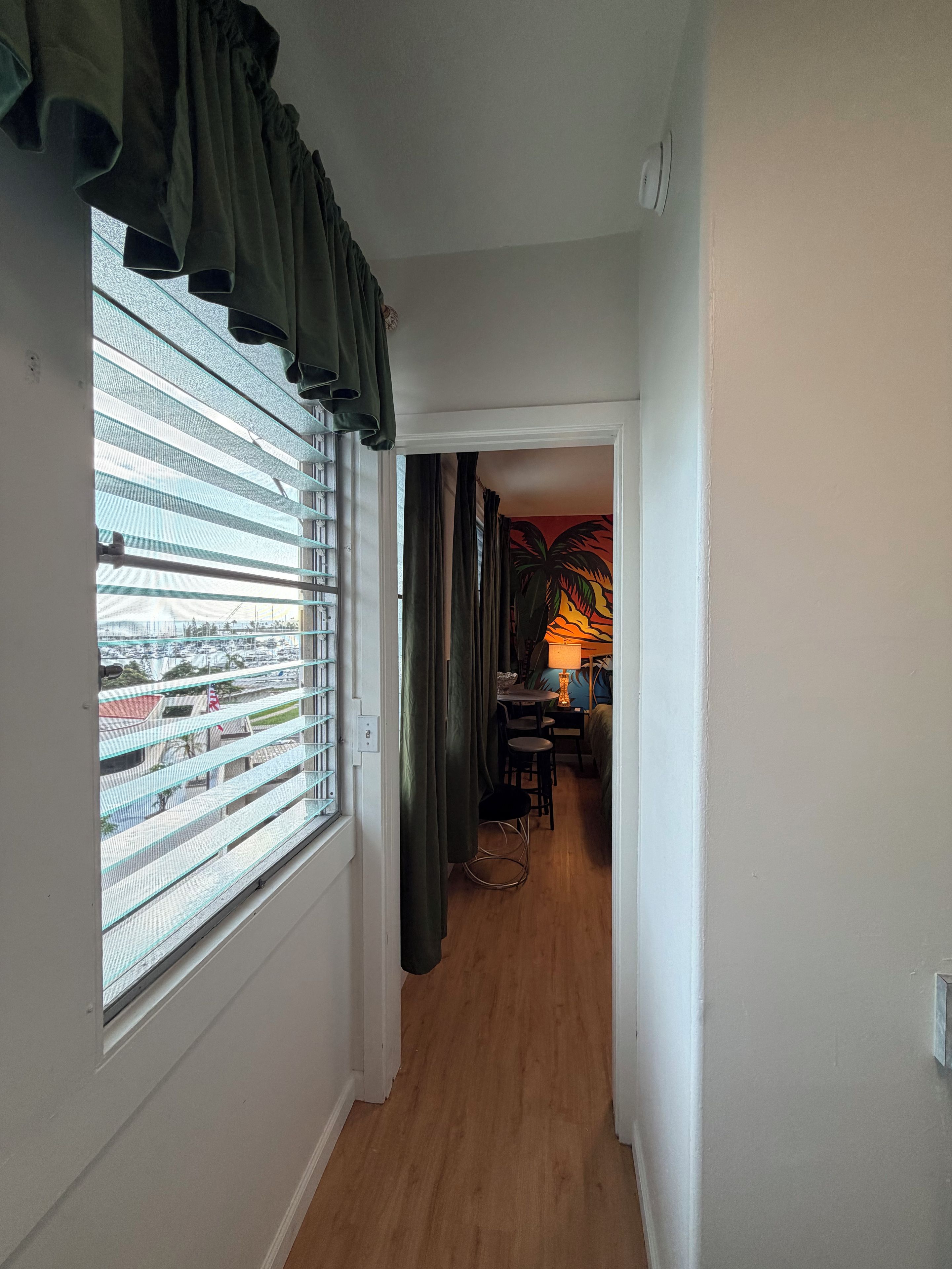 Un pasillo con ventana, vista hacia un puerto deportivo y un comedor con lámpara.