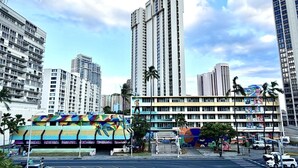 A multi-story building with a colorful mural on the lower level, surrounded by high-rise buildings. - Central YMCA Residences (Honolulu)