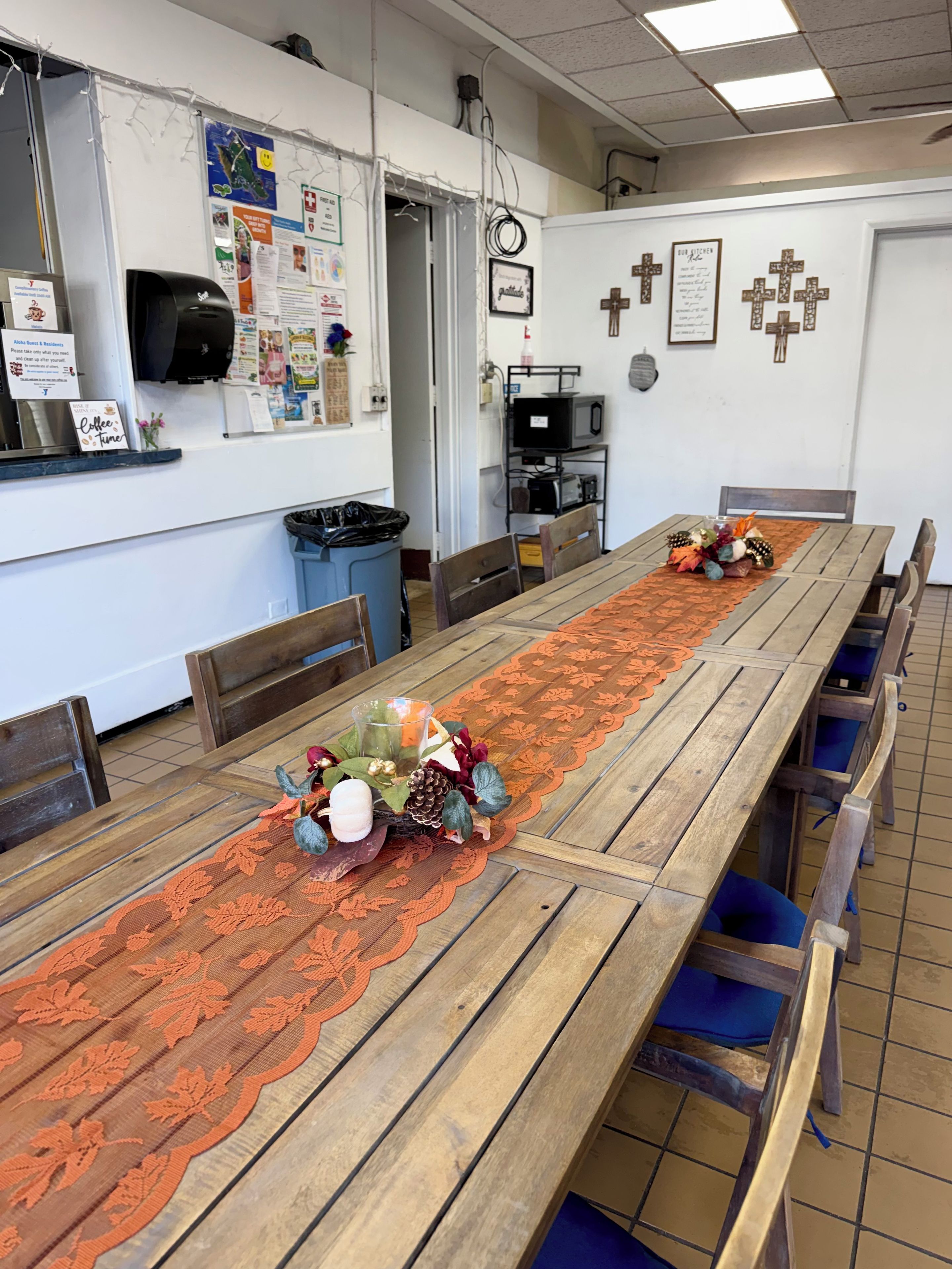 Een lange houten tafel met een decoratieve tafelkleed, omringd door stoelen.
