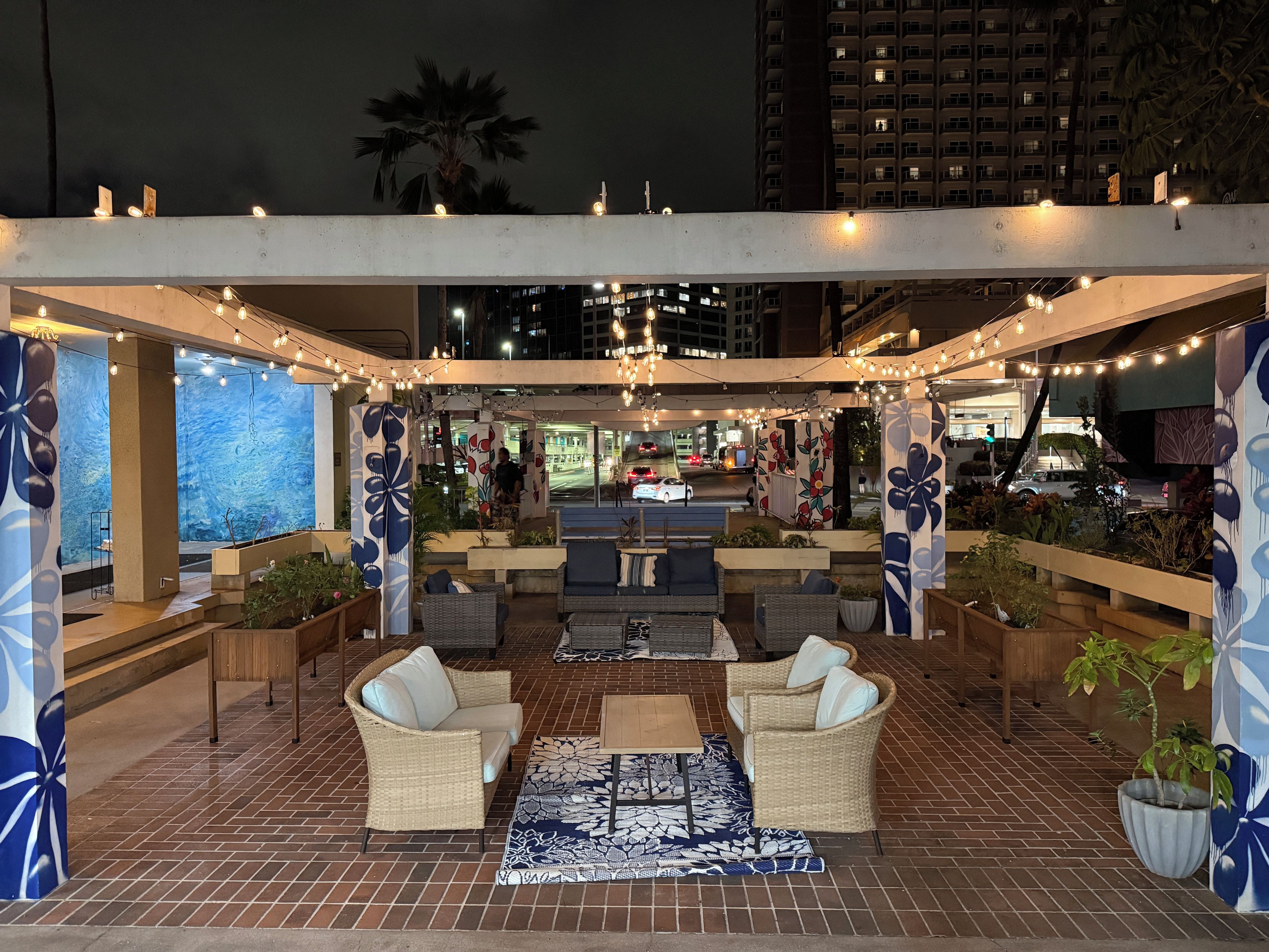 Un área de estar exterior con muebles de mimbre, alfombra estampada y luces colgantes.