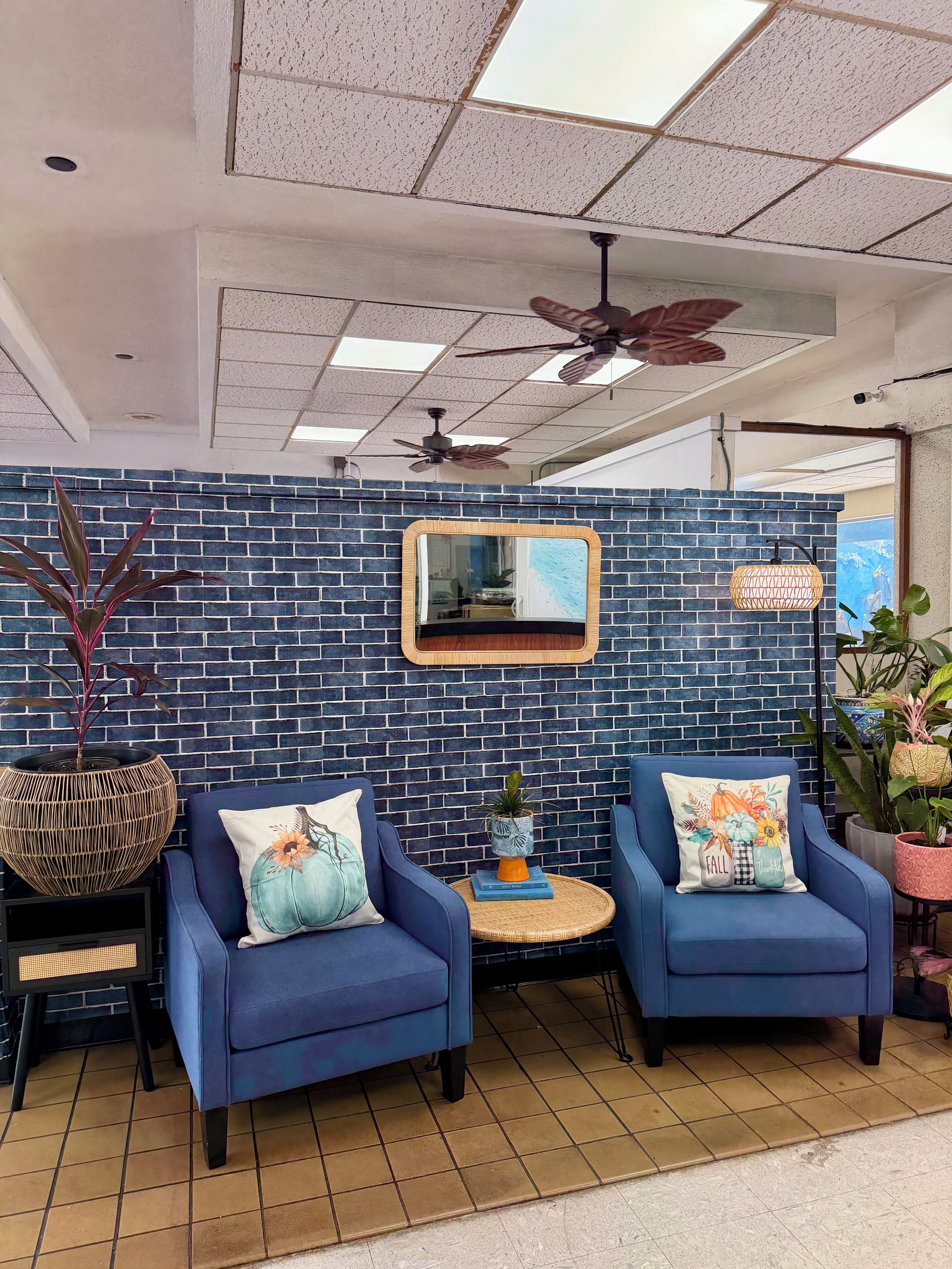 A seating area with two blue armchairs, a round table, and a decorative mirror on a brick wall.
