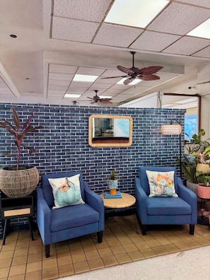 A seating area with two blue armchairs, a round table, and a decorative mirror on a brick wall. - Central YMCA Residences (Honolulu)