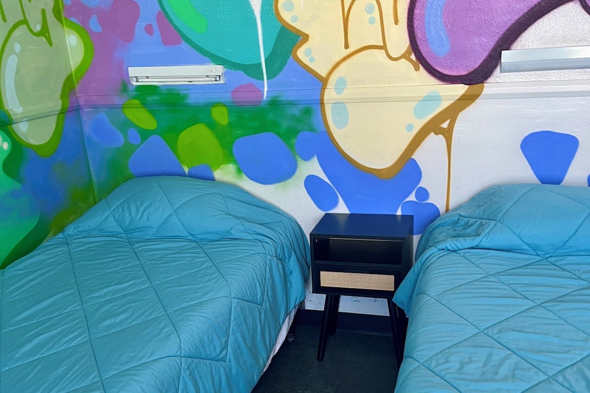 A room with two beds, a small table, and colorful graffiti on the walls.