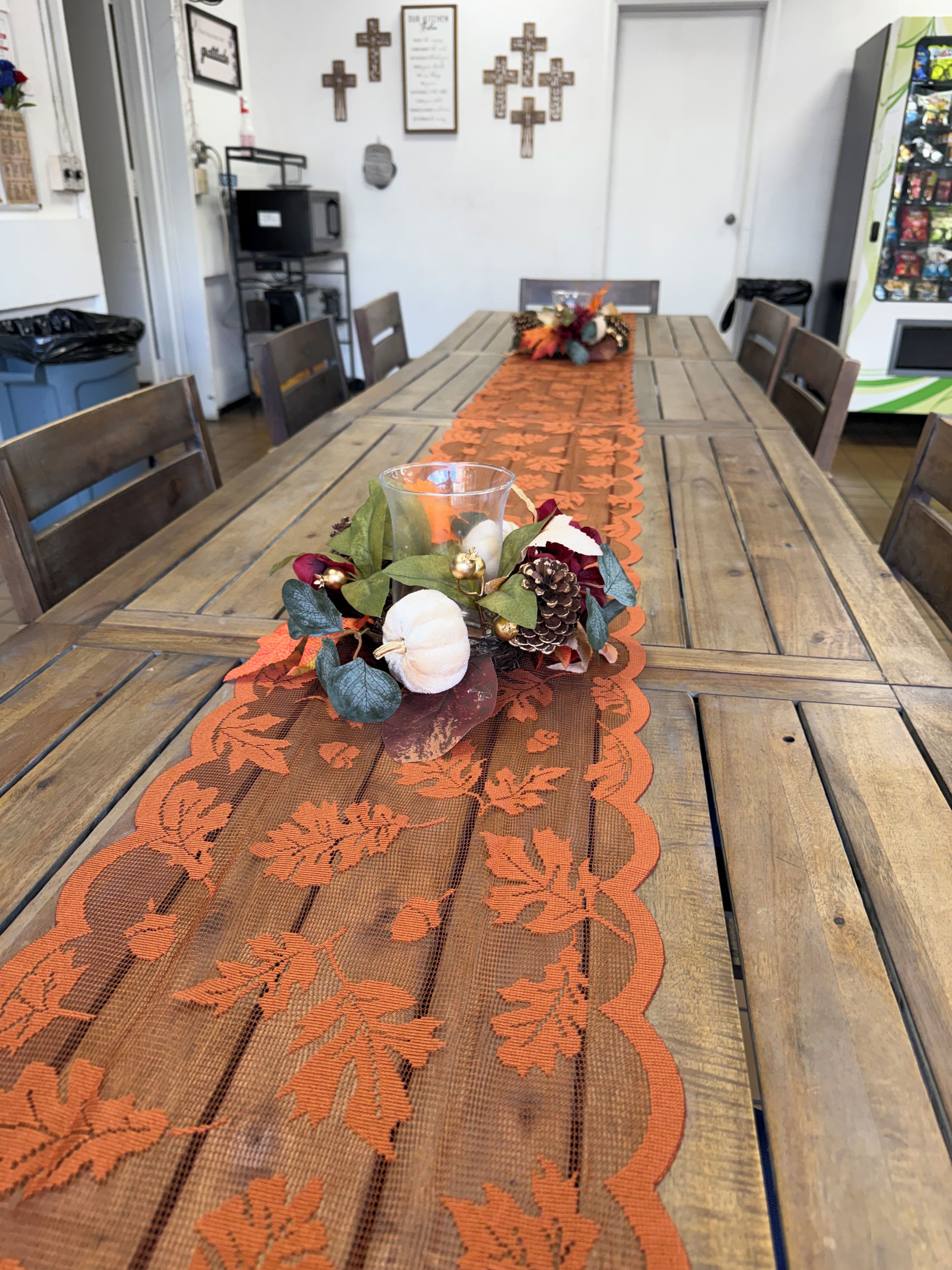 A dining table with a lace table runner, chairs, and a centerpiece with flowers and a candle.