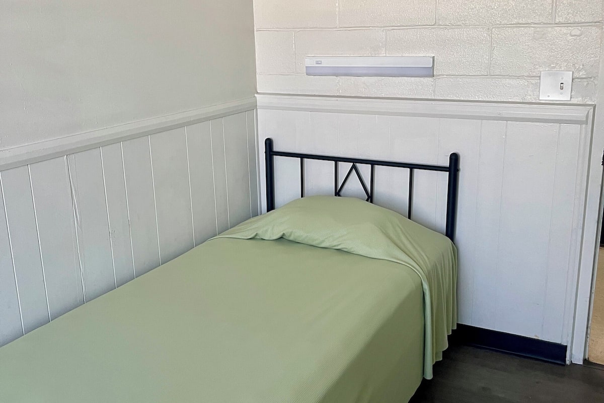 A single bed with a metal frame and green bedding in a room with white walls and a white brick accent wall.
