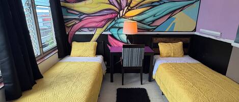 Una habitación con dos camas, un escritorio y un mural grande y colorido en la pared.