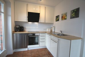 A compact kitchen with white cabinets, a Bosch oven, a coffee maker, and a sink. - Rungholtstraße 6, Whg. 1 (Wyk auf Föhr)