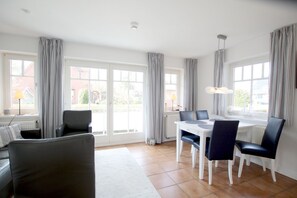 Uma sala de estar moderna com sofá, mesa de jantar, cadeiras e janelas grandes com cortinas.