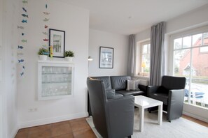 A living room with a sofa, chairs, a coffee table, a glass cabinet, and a window with curtains. - Rungholtstraße 6, Whg. 1 (Wyk auf Föhr)