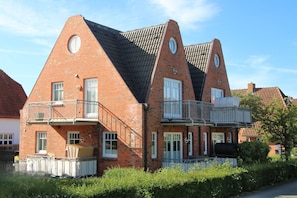 A two-story brick building with a unique triangular roof design, multiple windows, and a balcony. - Rungholtstraße 6, Whg. 1 (Wyk auf Föhr)