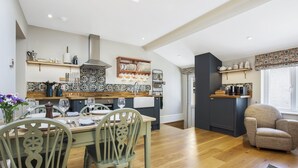 Una cocina moderna con armarios de madera, un comedor con mesa y sillas, y una zona de estar acogedora con una butaca.