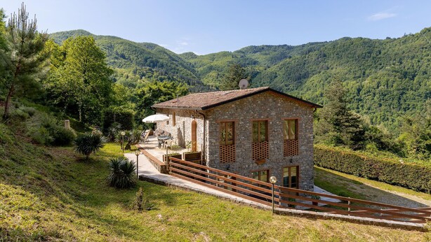 A stone house with a sloped roof, a small porch, and a view of lush green mountains. - Stunning apartment in Borgo a Mozzano (Borgo a Mozzano)