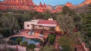 A house with a pool, surrounded by trees and red rock formations.