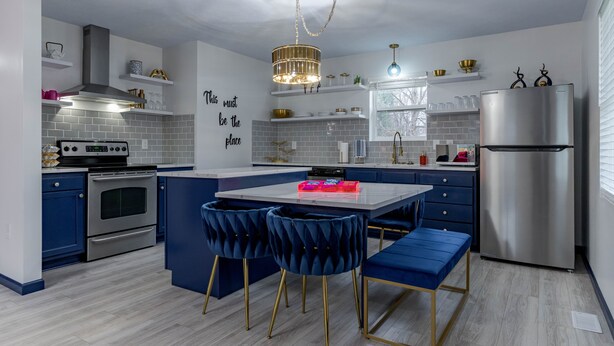 A modern kitchen with a central island, blue bar stools, a stainless steel refrigerator, and a decorative chandelier. - Sleek+ Modern Home Close to Downtown (Elizabethtown)