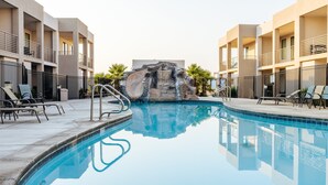 A swimming pool with a rock waterfall feature, surrounded by a fence and lounge chairs. - The Lofts 2|Community Pool w/water slide and hot tub, grill, Smart TV (Saint George)